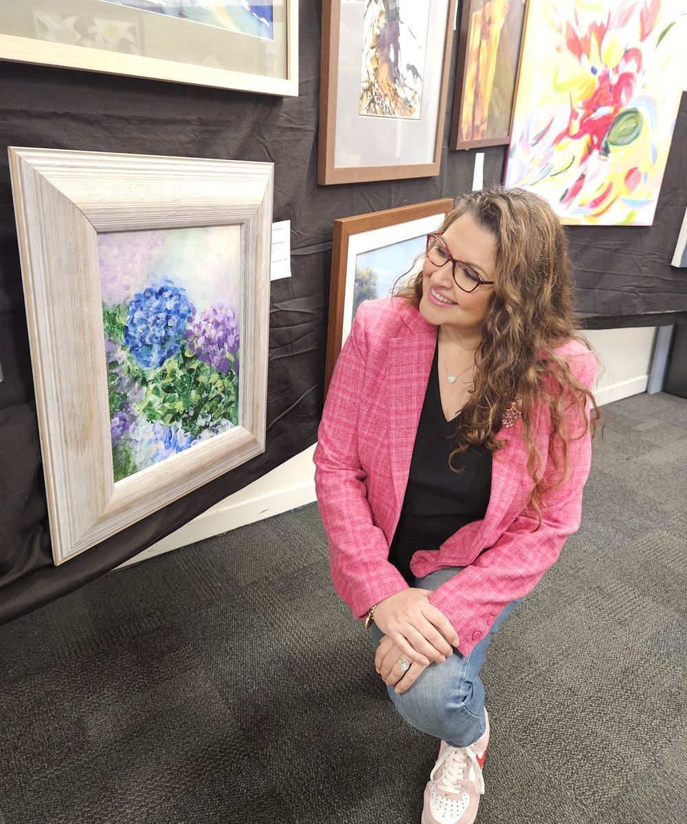 Natalie Gardner smiling beside her framed hydrangea painting at the Blackwood Rotary Art Show
