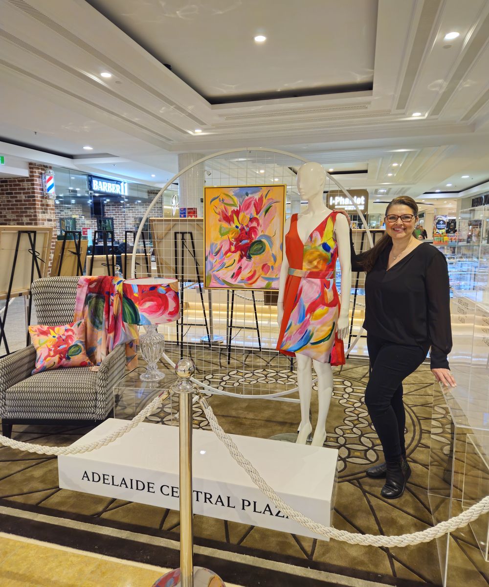 Natalie Gardner beside her Canvas and Beyond display at Adelaide Central Plaza, with a painting and a matching hand-finished dress on a mannequin