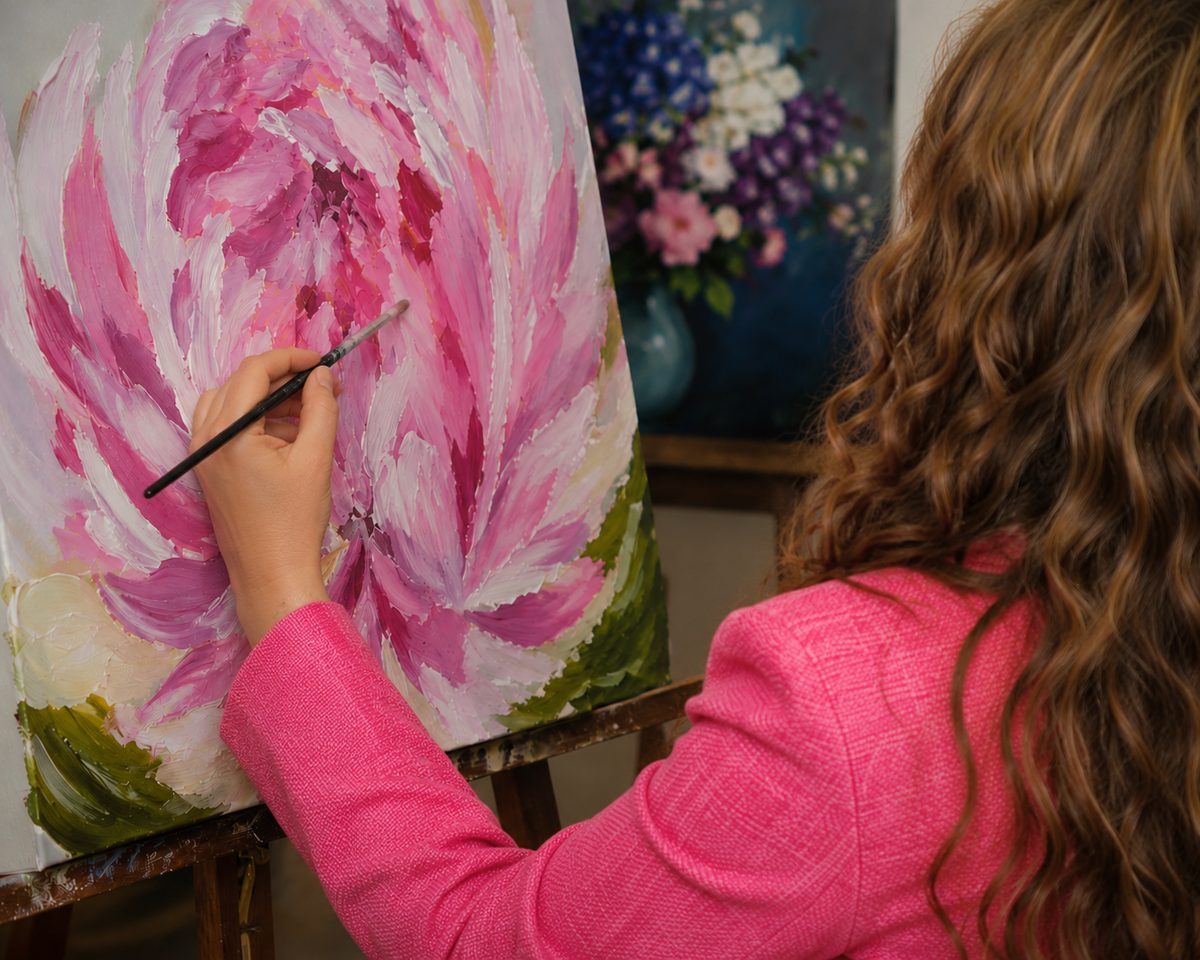 An artist painting a large pink peony at an easel